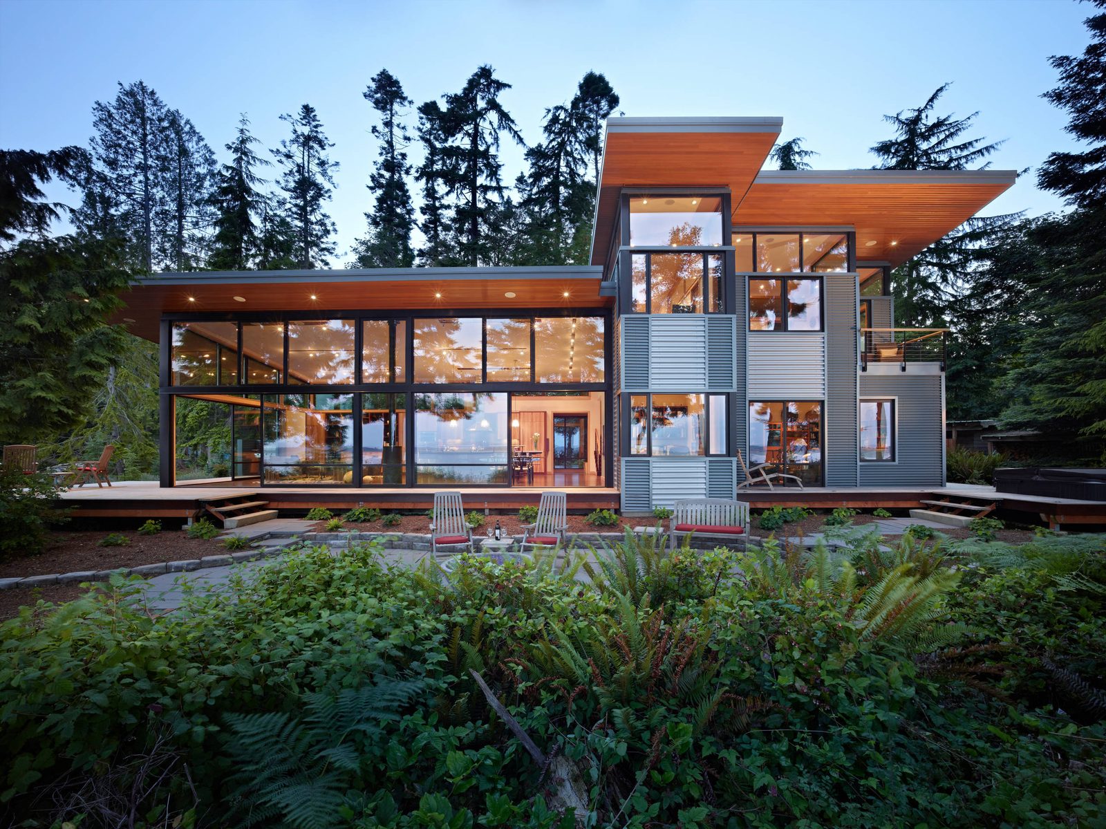 Modern glass home with floor-to-ceiling window walls and sliding glass doors at dusk